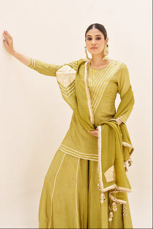 Woman wearing a green traditional outfit with white patterns on a beige background