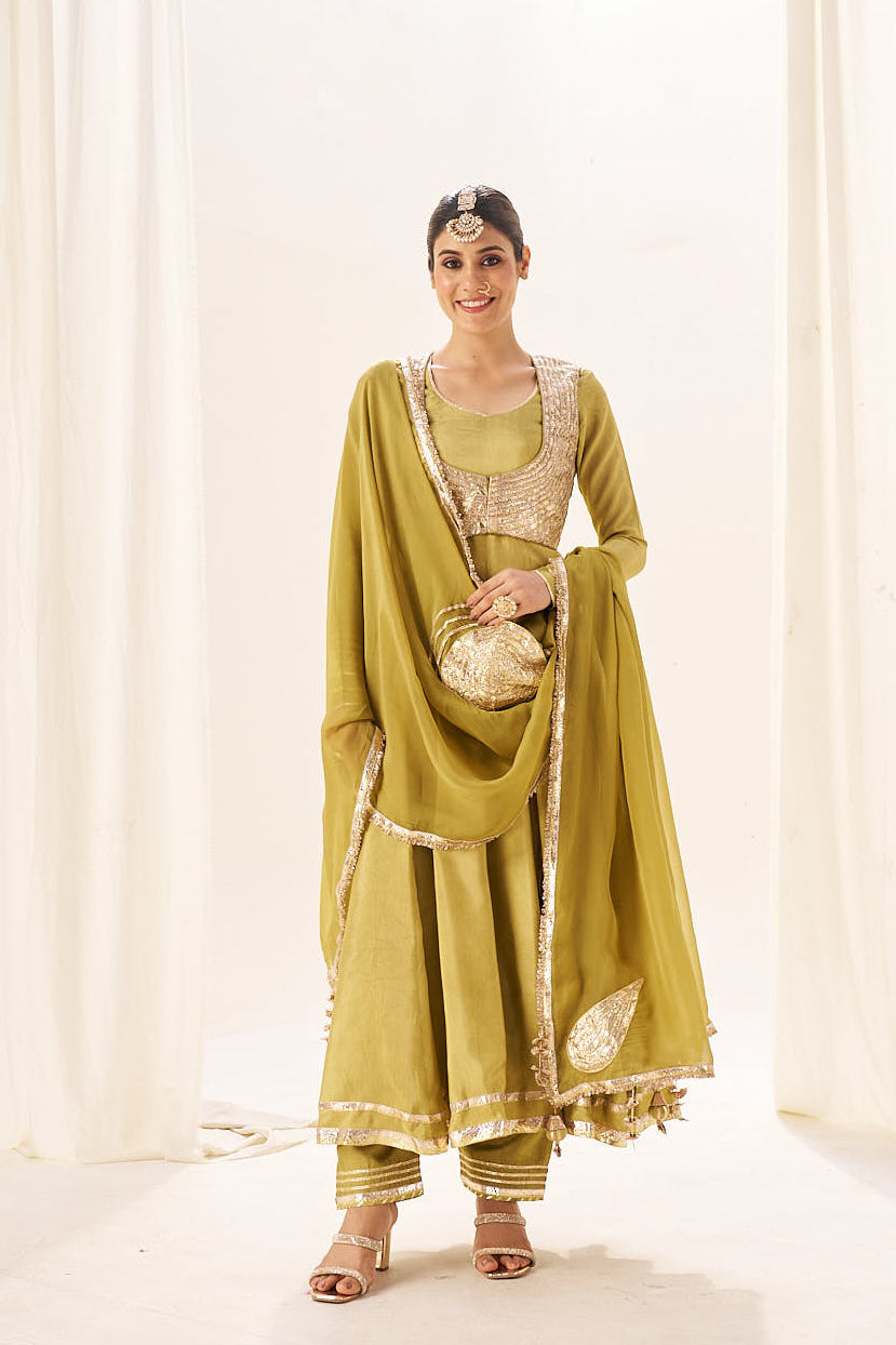 Woman wearing a green traditional outfit with a matching dupatta against a white curtain background