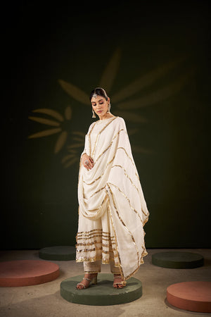 women in White Anarkali and chiffon dupatta with gotta laces standing in a dark background 